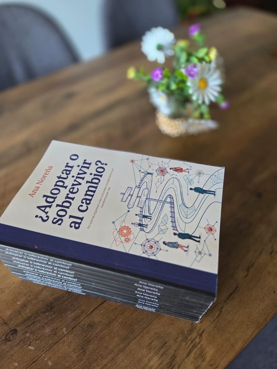 Printed copies of Ana Noreña's book ¿Adoptar o sobrevivir al cambio? on a wooden table